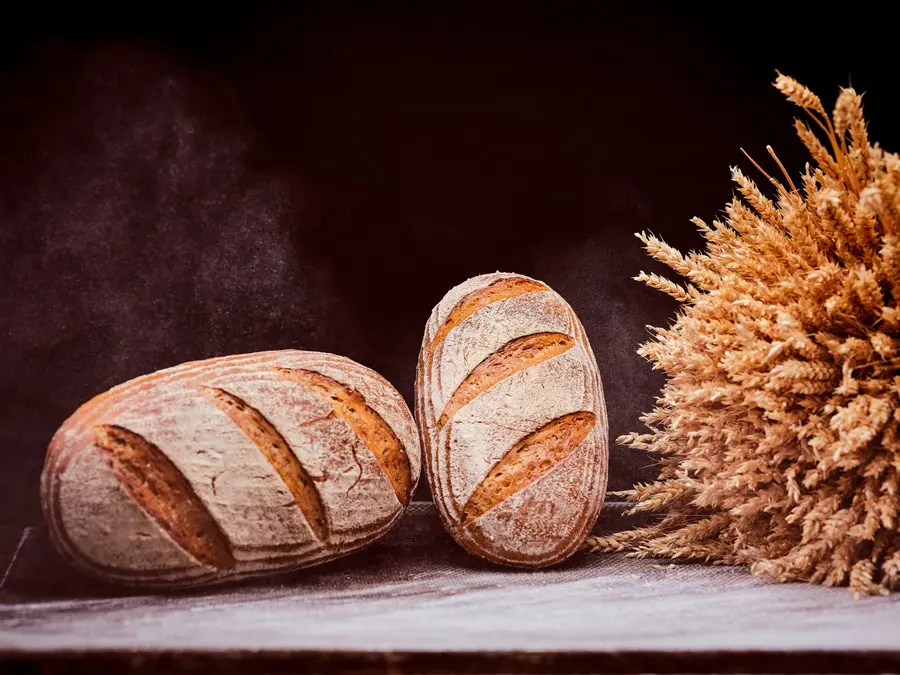 Zwei Brotlaibe mit Mehlstaub neben einem Bündel Getreideähren